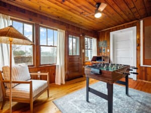 Bright game room with foosball table overlooking sunlit living space and rolling wooded forest views.