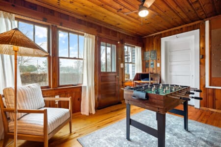 Bright game room with foosball table overlooking sunlit living space and rolling wooded forest views.