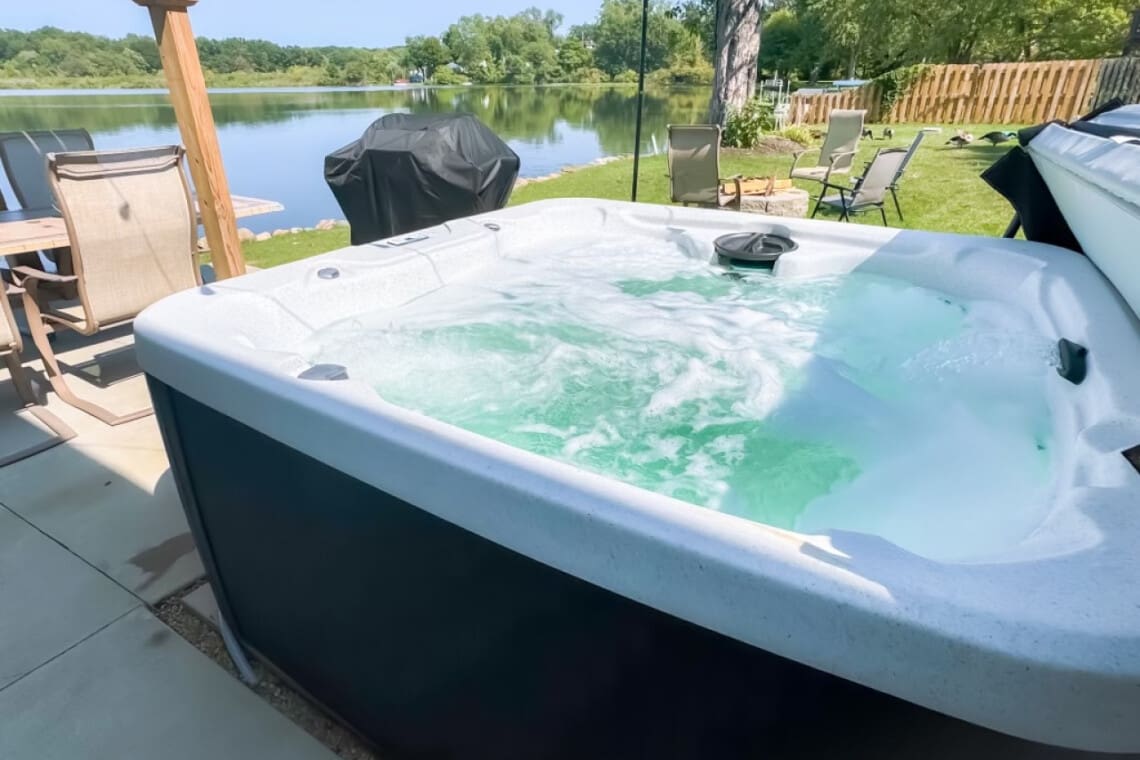 Scenic lakeside yard with hot tub and grill, offering stunning water views and relaxing outdoor amenities.