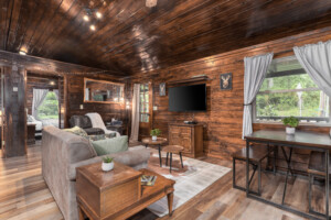 Rustic Cabin Living Room with Wooden Interior and Mounted TV Cozy cabin living room with wooden walls, mounted TV, rustic furniture, and large windows with natural light