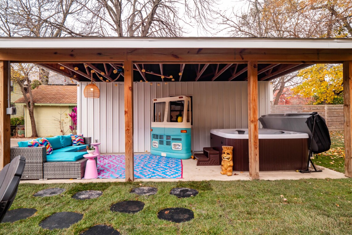 Resort-style short-term rental backyard with hot tub, fire pit seating, VW bus mini bar, string lights, and outdoor entertainment space