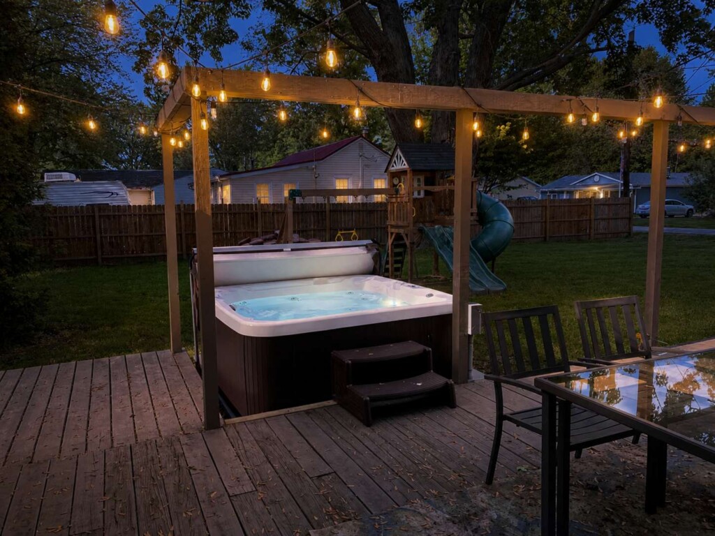 Inviting short-term rental backyard with hot tub, outdoor seating, and colorful evening lighting for guests